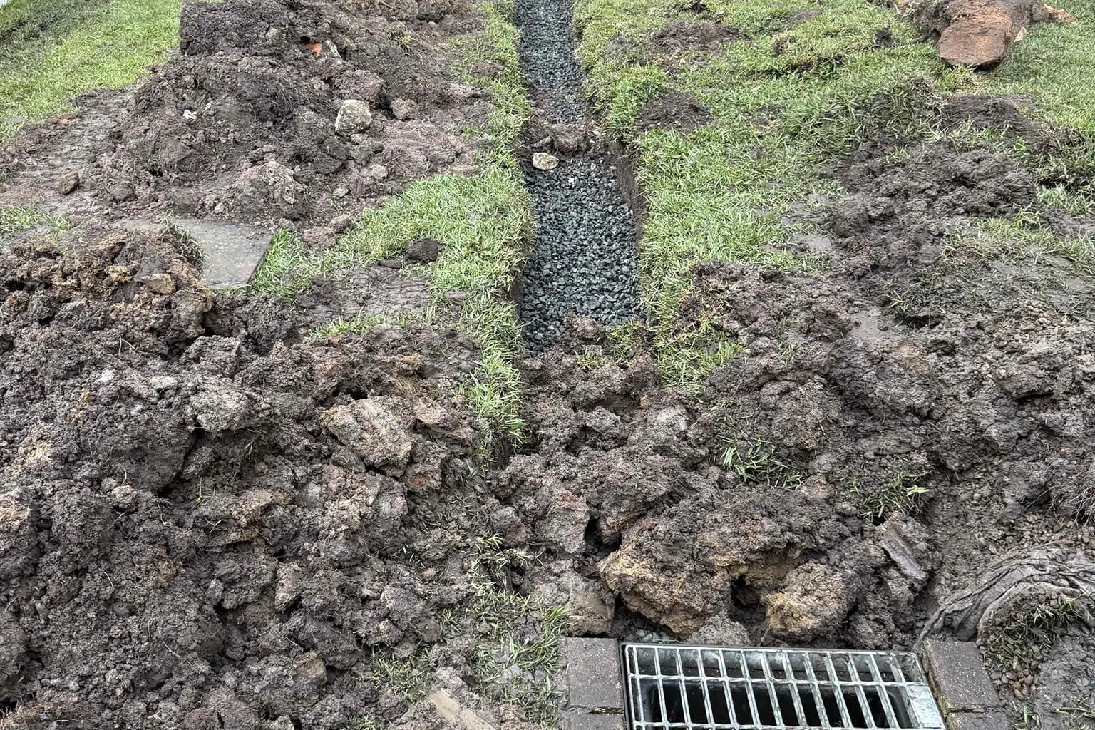 Trench dug across a backyard to a stormwater grate