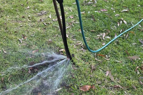 Burst pipe at a garden tap spraying water across a lawn