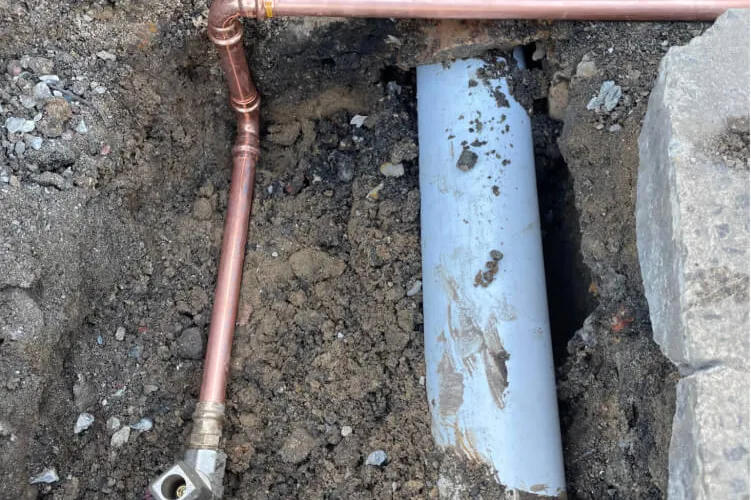 Copper gas line exposed in an excavation beside a PVC pipe