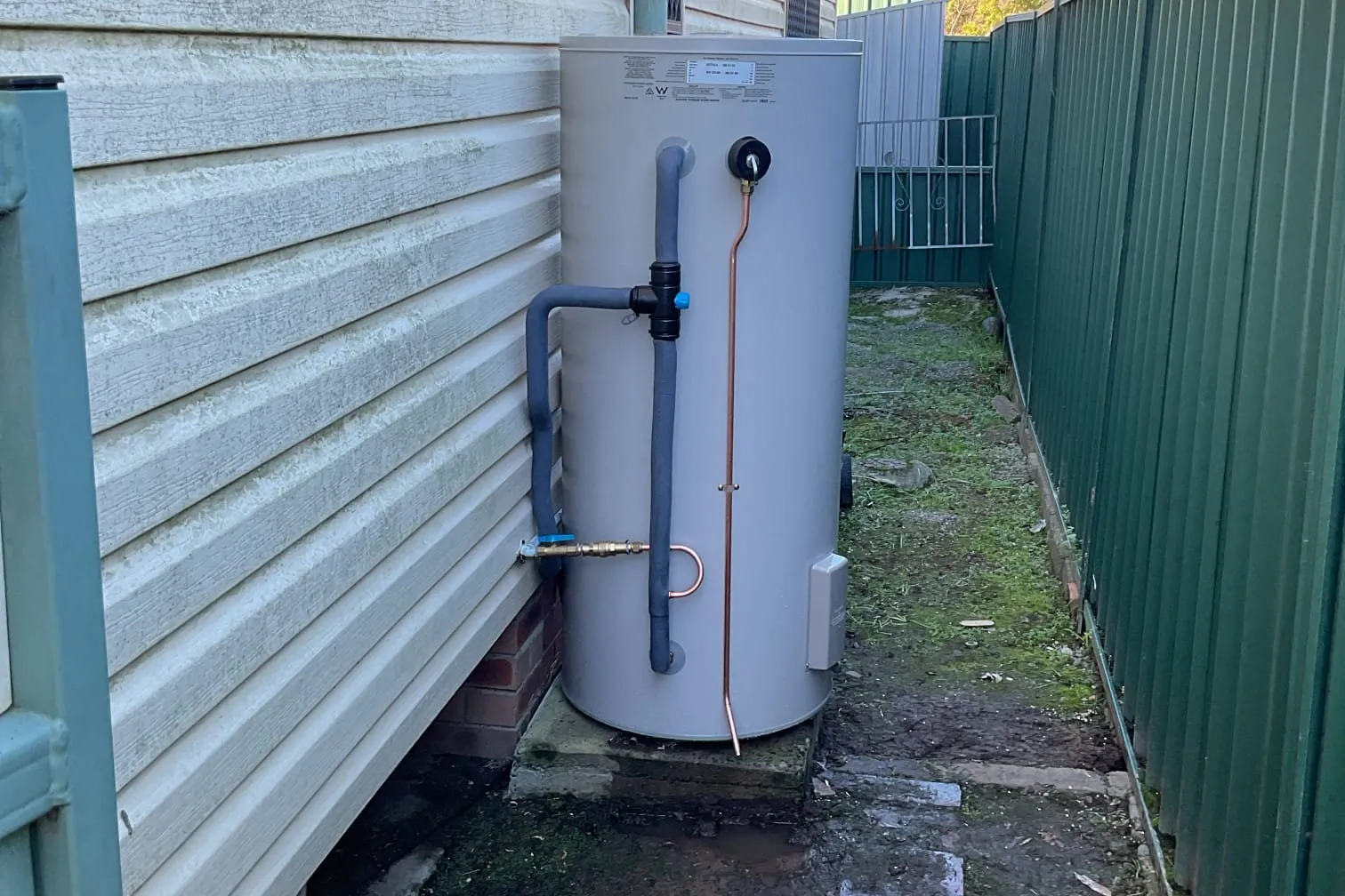 Electric hot water system beside a weatherboard house