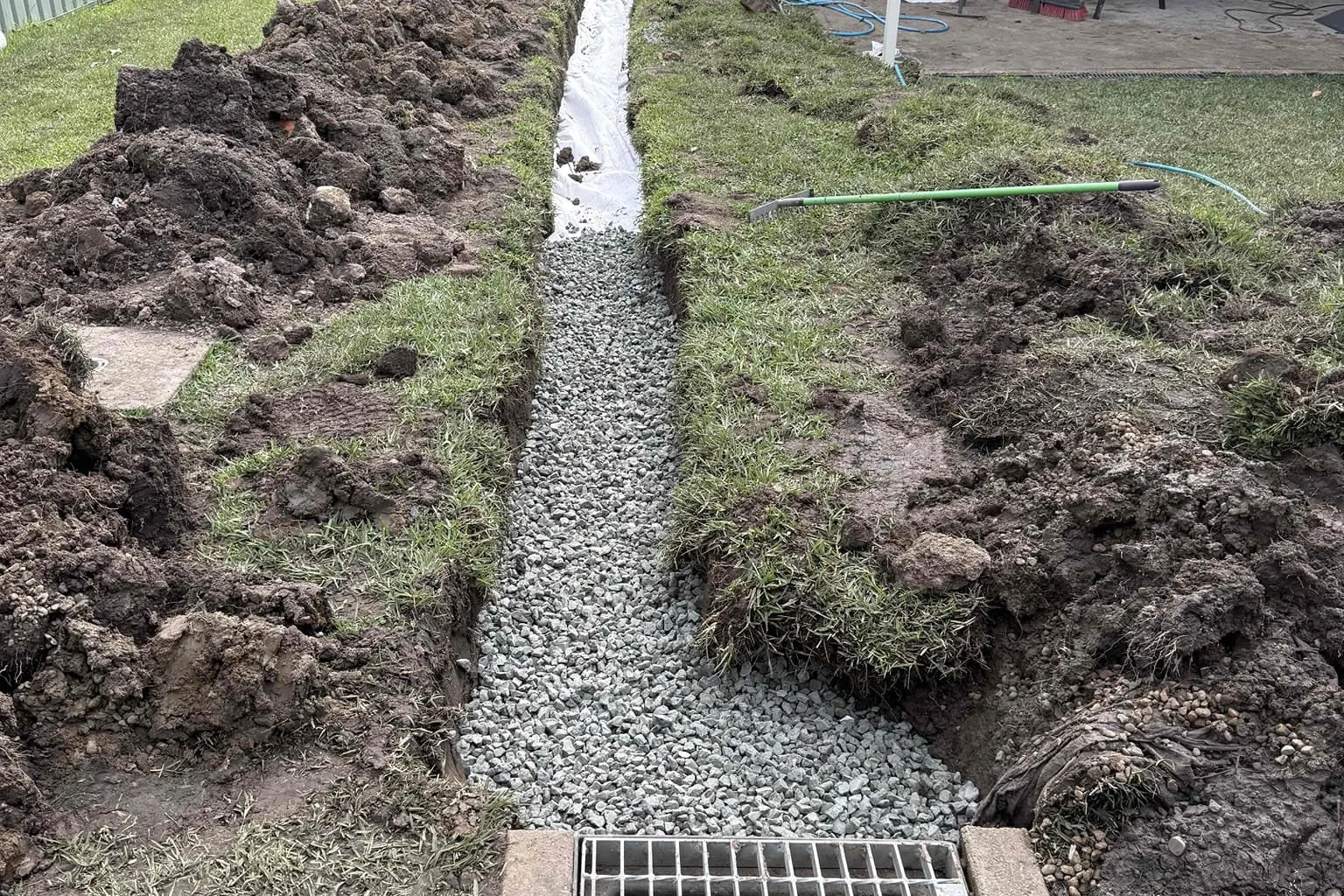 Gravel drainage trench leading to a stormwater grate