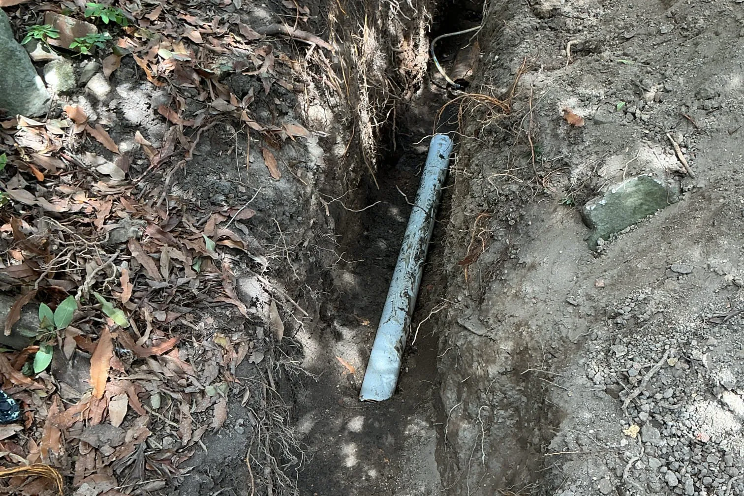 Trench through a garden bed exposing a sewer line and inspection opening