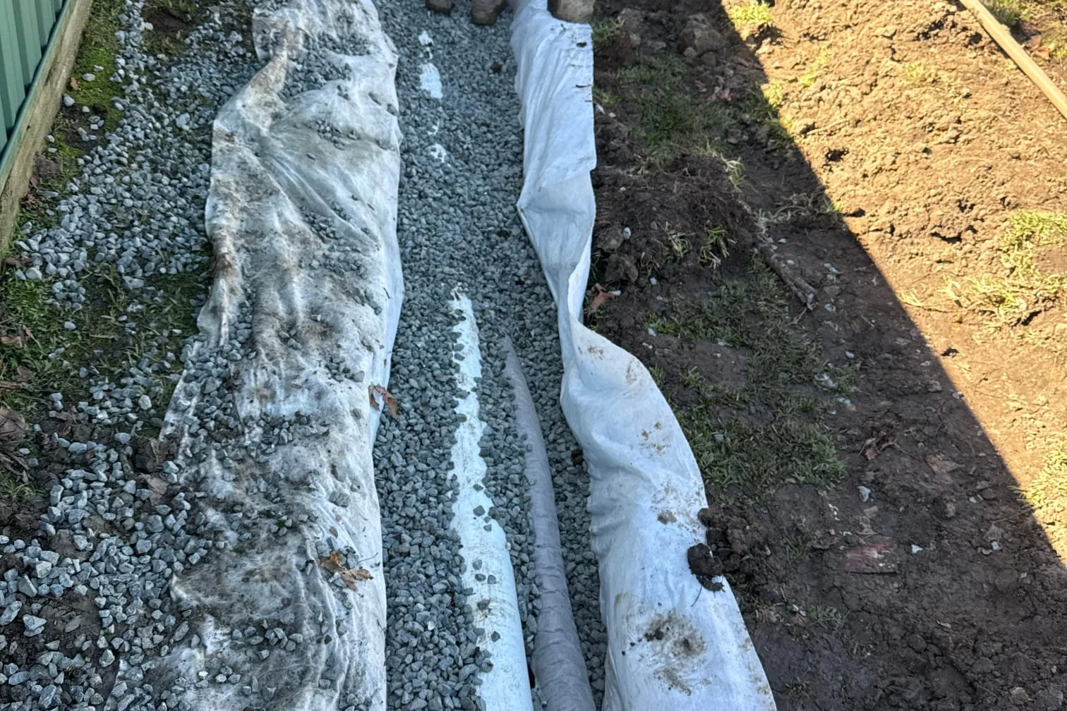 Subsoil drainage pipe wrapped in filter fabric in a gravel trench